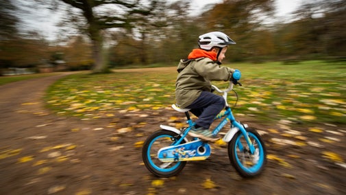 Child riding a bike on a track with autumn leaves on the ground